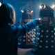 The Doctor waves her sonic screwdriver at three approaching Daleks.